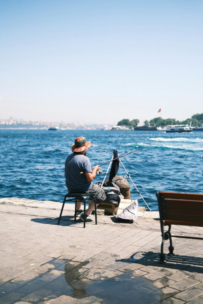 A man fishing by the sea on a sunny day, enjoying a peaceful outdoor moment.